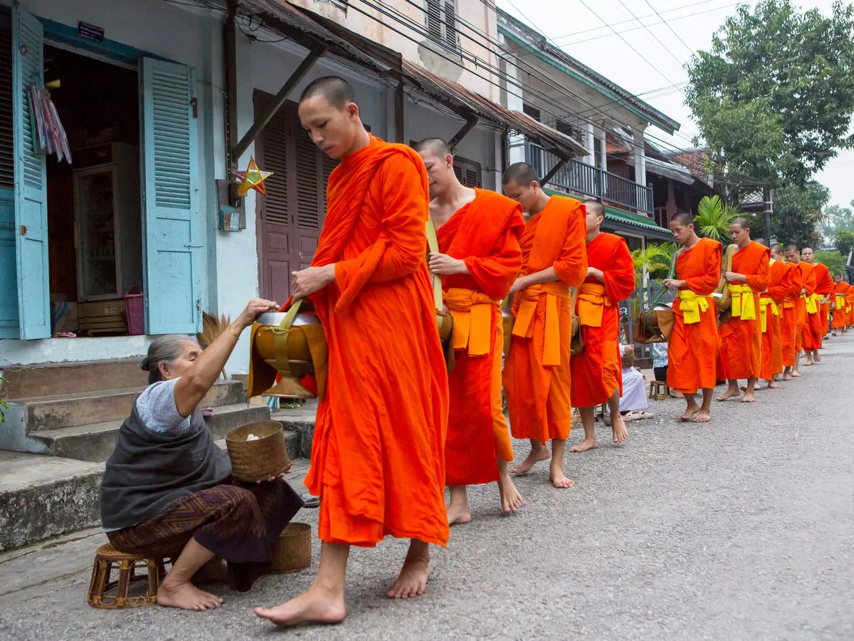 a woman offers alms to a procession of buddhist mo 2025 04 03 18 06 23 utc